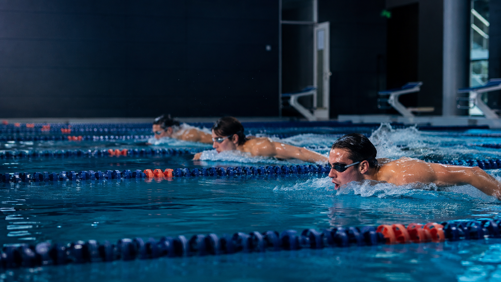 Nadadores adolescentes y jóvenes entrenando en una piscina cubierta